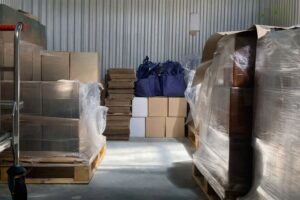 Lagergång med pallar fyllda med kartonger, några med blåa tygväskor.