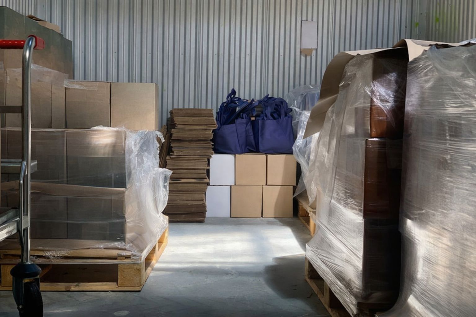 Lagergång med pallar fyllda med kartonger, några med blåa tygväskor.