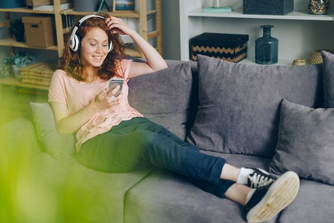 Kvinna med hörlurar väljer musik på mobilen i soffan
